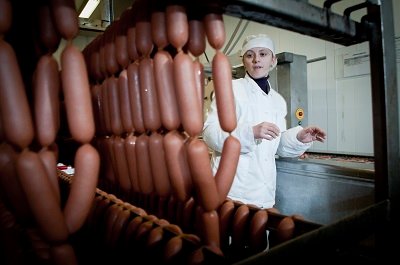 Pølsemaker hos Mydland foran rekker med røkte pølser